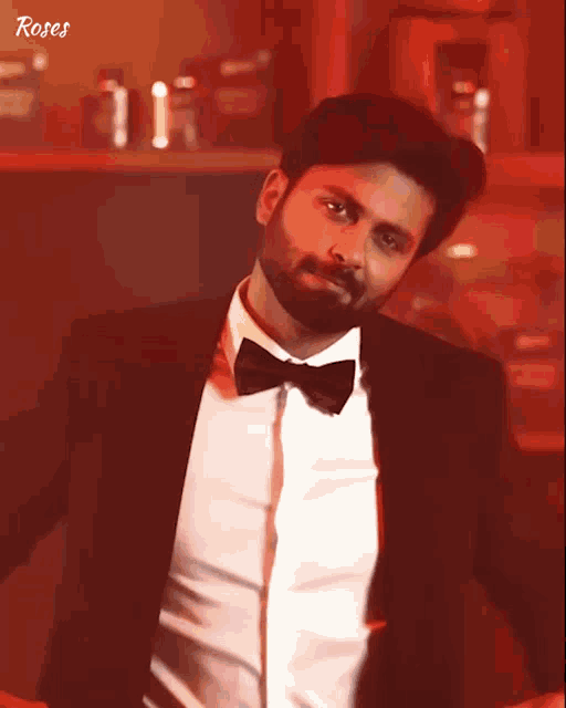 a man with a beard wearing a tuxedo and bow tie with roses written on the bottom right