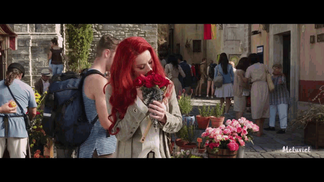 a woman with red hair is smelling a bouquet of roses in a crowd