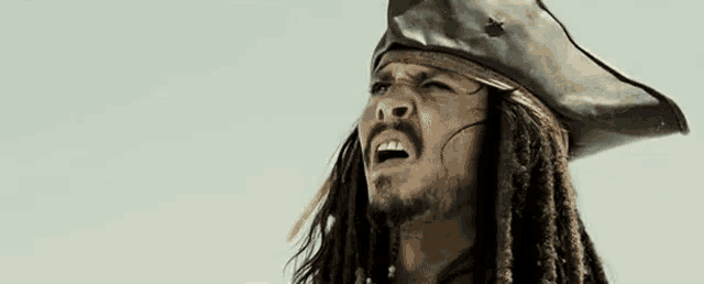 a man with dreadlocks is wearing a pirate hat and making a face .