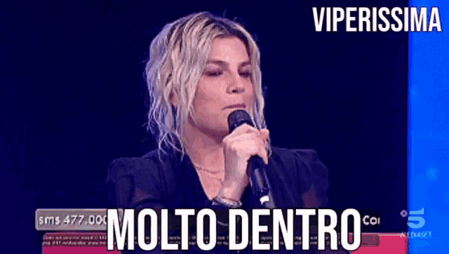 a woman singing into a microphone with molto dentro written on the screen behind her