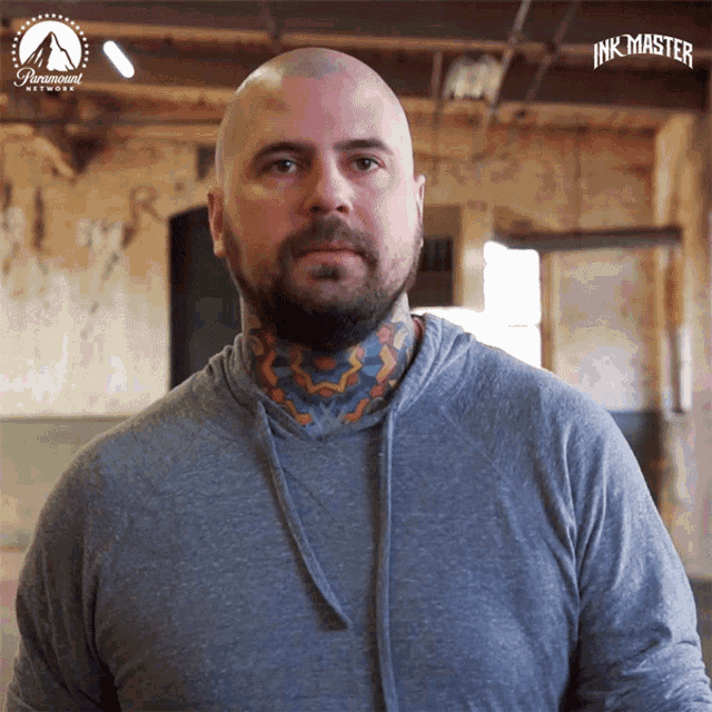 a man with a tattoo on his neck is wearing a grey shirt with the word inkmaster on it