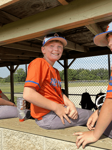 a boy wearing an orange shirt with the word angels on it sits on a bench