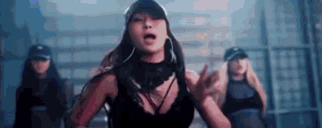 a woman in a black tank top and hat is dancing in a dark room .