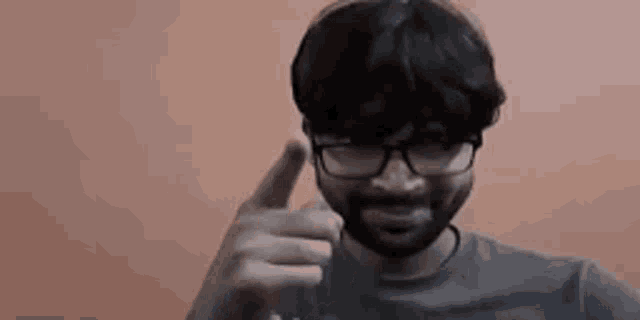 a man with glasses and a beard is pointing his finger at the camera .