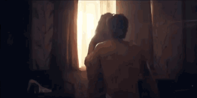 a man and a woman kissing in front of a window .