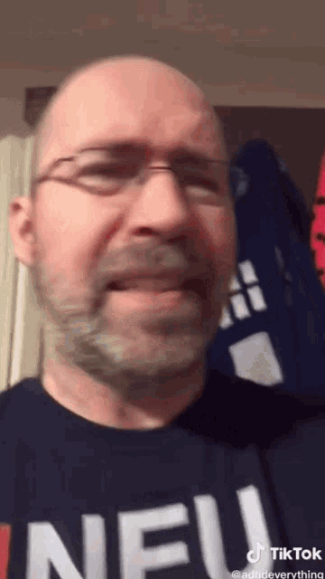 a bald man with glasses and a beard is wearing a shirt that says neu on it