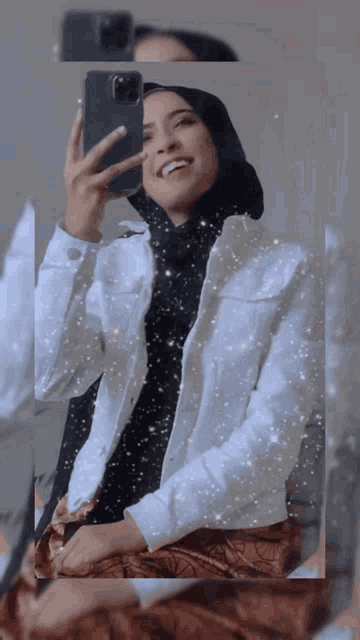 a woman in a hijab takes a selfie with her phone