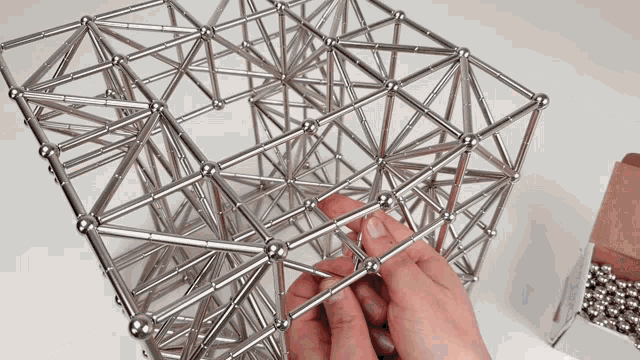 a person is playing with a metal structure that looks like a cube