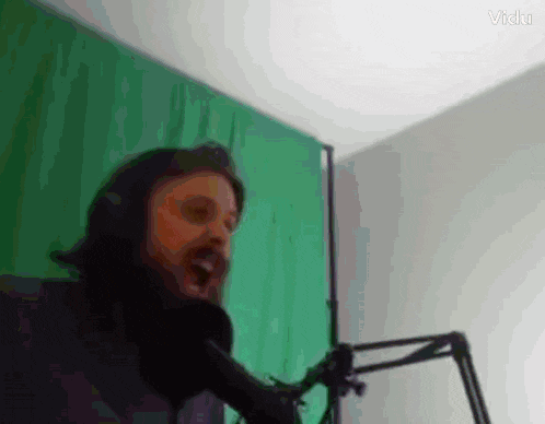 a man singing into a microphone in front of a green wall
