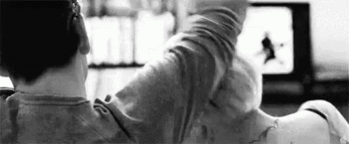 a black and white photo of a man laying on a woman 's lap while watching a television .