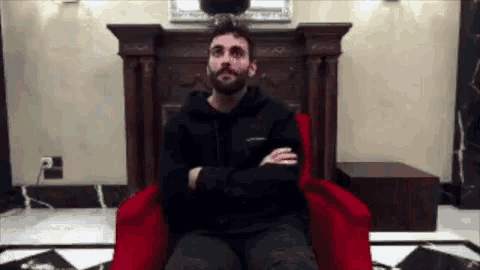 a man in a black hoodie is sitting in a red chair with his arms crossed