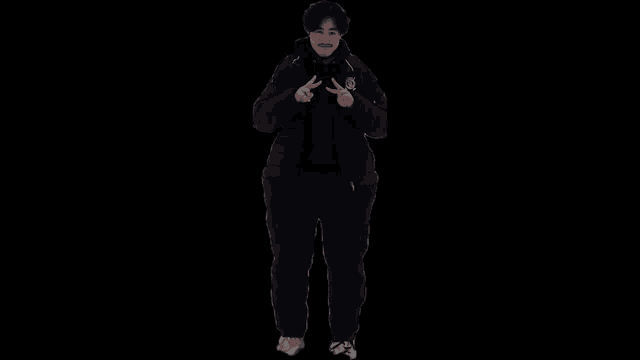 a man in a black jacket and black pants is making a peace sign