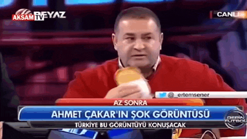 a man is eating a hamburger in front of a tv screen that says aksam tv