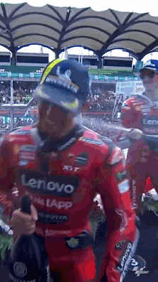 a man in a red lenovo motorcycle suit is standing in front of a crowd holding a bottle of champagne .