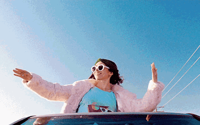 a woman wearing sunglasses and a pink fur coat is sitting in the back of a car with her arms outstretched