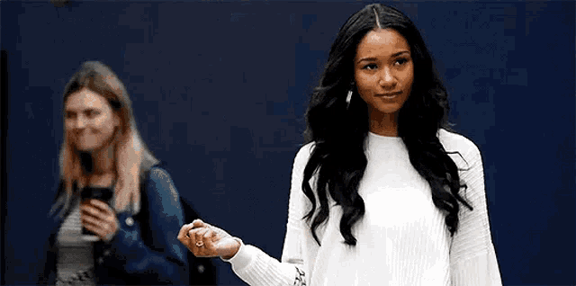a woman in a white sweater is standing in front of a blue wall with another woman in the background .