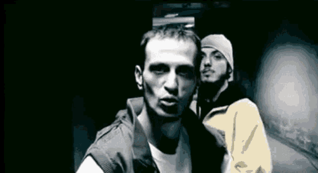 two men are standing next to each other in a dark room looking at the camera