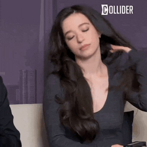 a woman with long dark hair is sitting on a couch with her eyes closed and holding her hair .