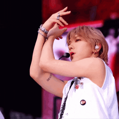 a young man wearing a white tank top is singing into a microphone in front of a crowd