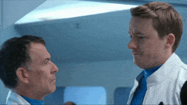 two men are looking at each other and one of them is wearing a white jacket