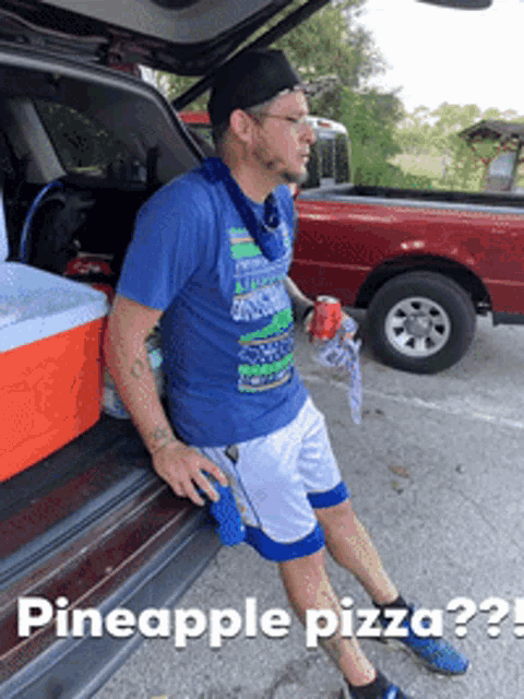 a man in a blue shirt is sitting in the back of a car with pineapple pizza written below him