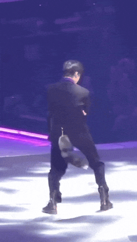a man in a black suit is dancing on a stage with purple lights behind him