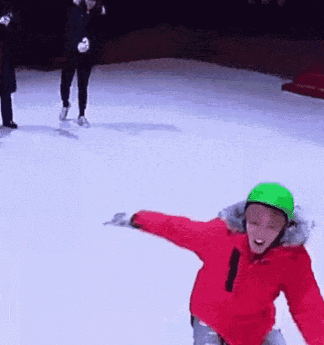 a young boy wearing a green helmet is ice skating on a rink .