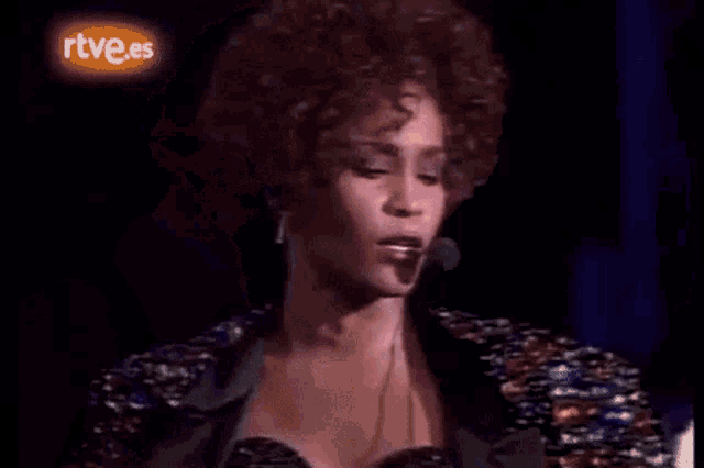 a woman in a wig is singing into a microphone on a stage .