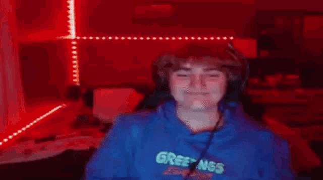 a young man in a blue hoodie is giving the middle finger while sitting in front of a red light .