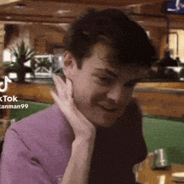 a man in a purple shirt is smiling with his hand on his face .