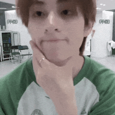 a young man wearing a green and white shirt is making a funny face
