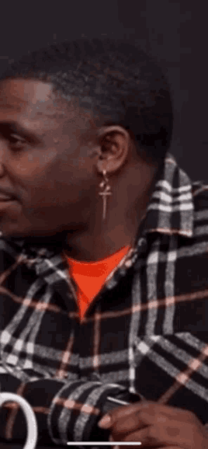 a close up of a man wearing a plaid shirt and earrings .