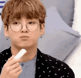 a young man wearing glasses and earrings is eating a stick of food .