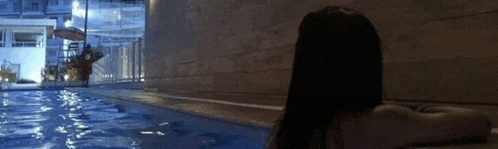 a woman is sitting on the edge of a pool at night