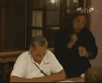 two men are sitting at a table and one has the word realty on the bottom right