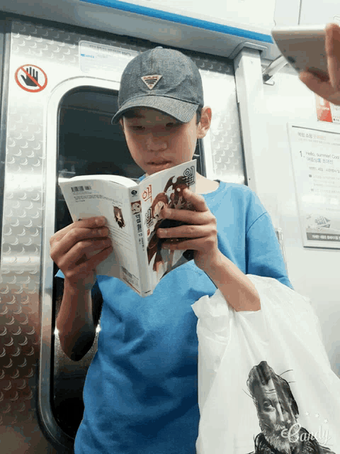 a boy wearing a prada hat is reading a book on a subway