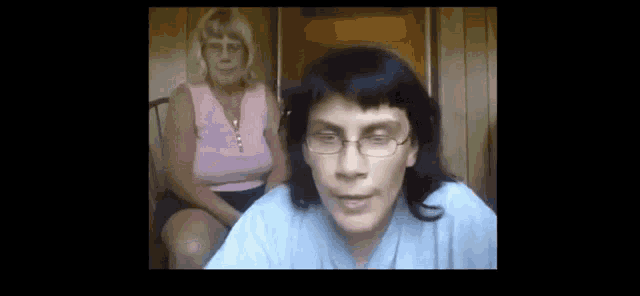 a woman wearing glasses looks at the camera while another woman sits in the background .