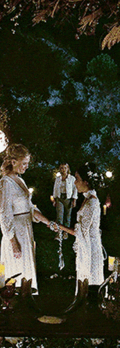 two women in white dresses are holding hands in a dark room