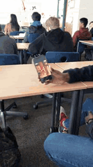 a person is holding a cell phone in a classroom with other students