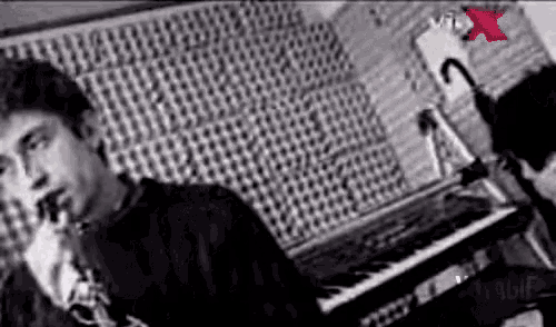 a black and white photo of a man playing a keyboard in a recording studio .