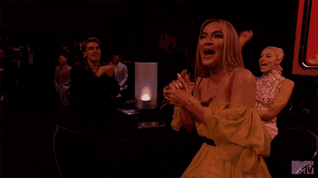 a woman in a yellow dress is applauding in front of a mtv sign