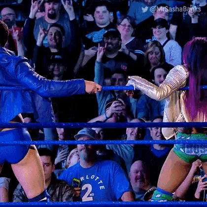 a woman in a blue jacket is standing in a wrestling ring with a crowd watching .