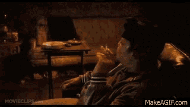 a man is smoking a cigarette while sitting on a couch in a living room .