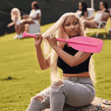 a woman is holding a pink paddle in her hand while sitting on the grass .