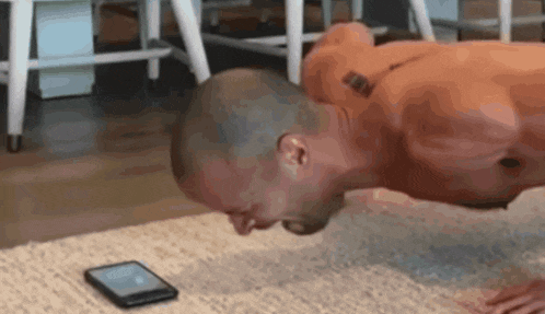 a shirtless man is doing push ups while a cell phone sits on the floor