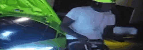 a man in a white shirt is standing next to a green car with the hood open .
