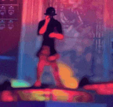 a man in a top hat is singing into a microphone in a dark room