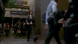 a man in a suit and tie is walking down a street in front of a building that has the word thompson on it