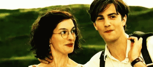 a man and a woman are standing next to each other in a field . the woman is wearing glasses .