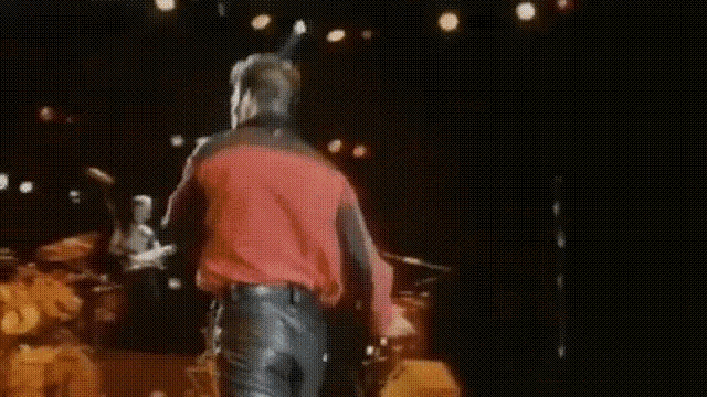 a man in a red shirt and leather pants is standing on a stage .